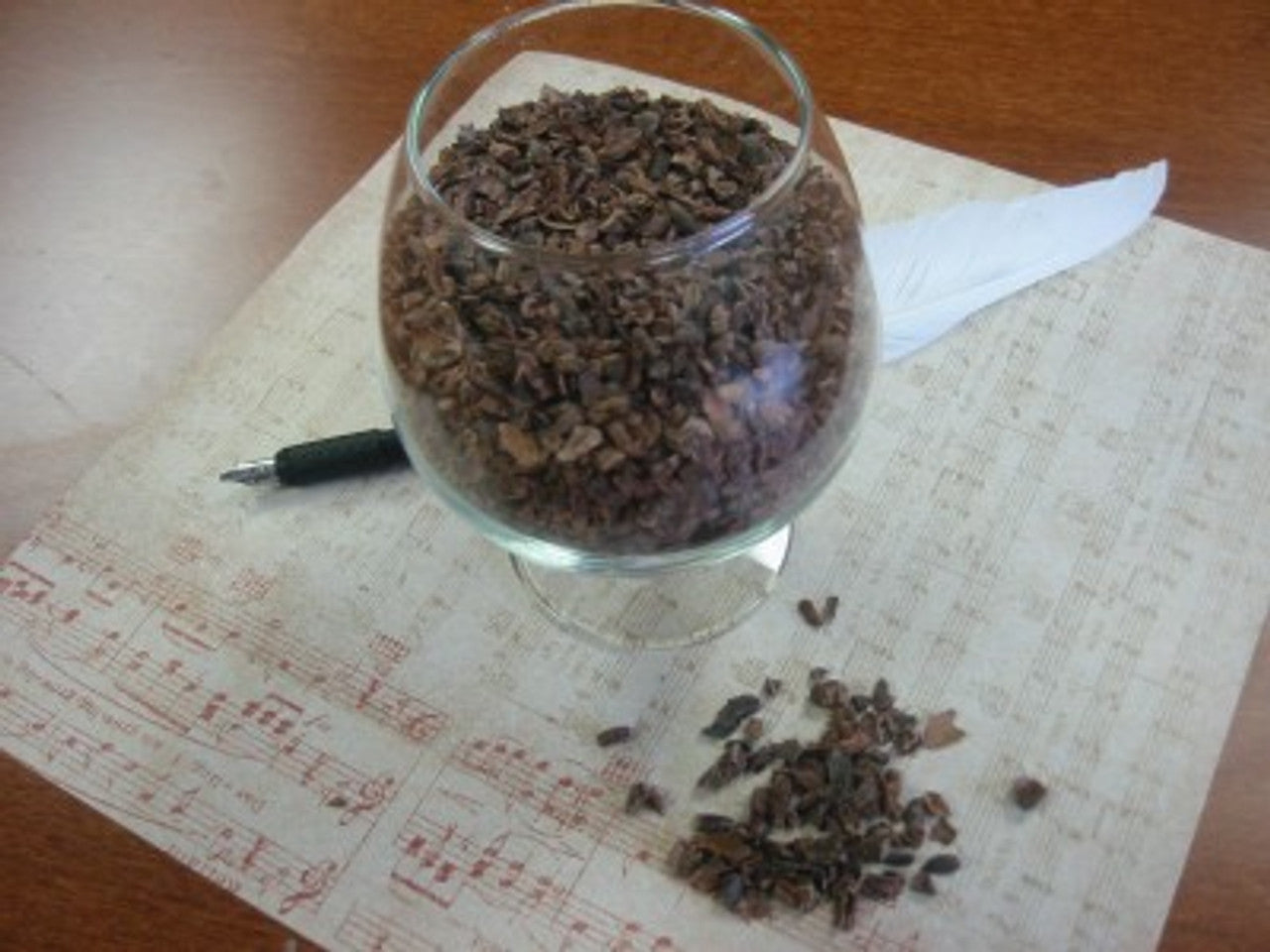 Cocoa Supply Ecuador Single Origin-Made Organic Raw Cacao nibs in a glass on a sheet of music with a feather pen